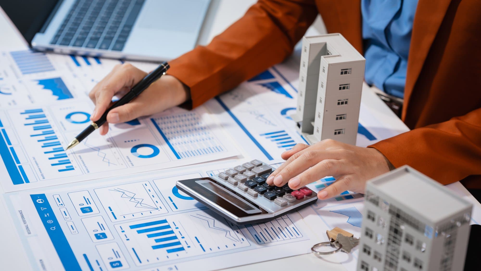 Commercial property manager reviewing financial performance reports with a calculator next to a model office building