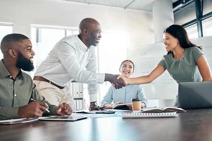 four individuals at a conference room table with two of them shaking hands