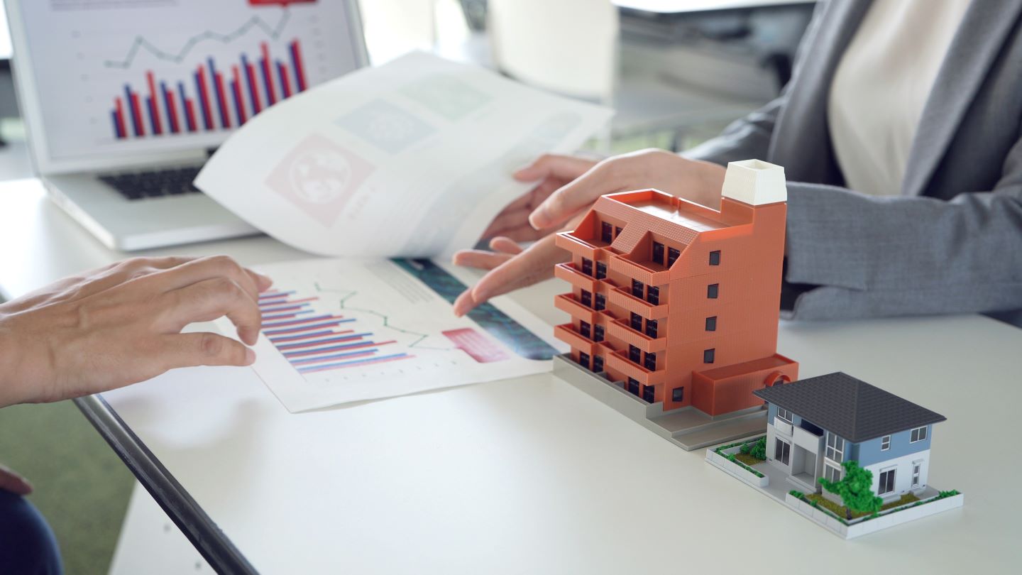 Investors & planners planning a CRE portfolio while examining an architectural model of multifamily (possibly commercial or mixed-use) & single-family residential structures.